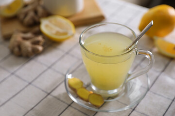 Glass of aromatic ginger tea and ingredients on white checkered tablecloth, closeup. Space for text