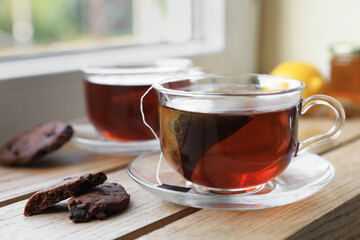 Bag of black tea in cups on wooden table indoors