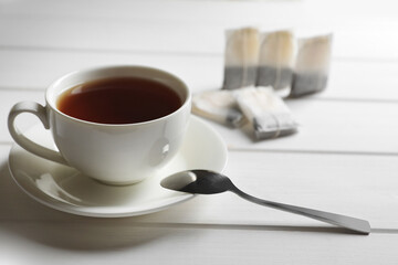 Tea bags near cup of hot drink on white wooden table. Space for text