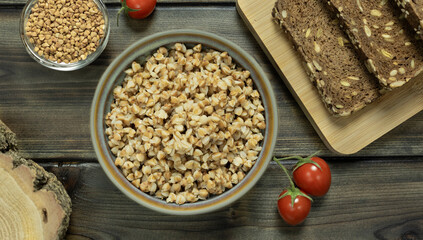 buckwheat porridge in a plate with rye bread, lettuce leaves and cherry tomatoes on a dark wooden background close-up.