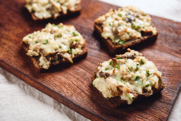 Rye bread toast with smoked mackerel, cream, cheese and green onion on wooden cutting board. Delicious appetizer, tapas. Selective focus - 548730121