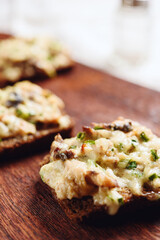 Rye bread toast with smoked mackerel, cream, cheese and green onion on wooden cutting board. Delicious appetizer, tapas. Selective focus - 548730123