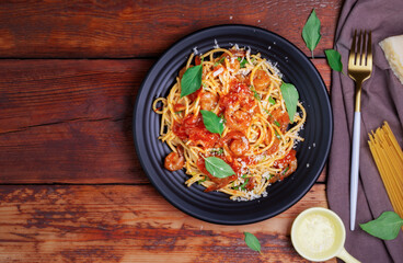 Delicious spaghetti pasta with prawns and cheese served on a black plate on a wooden table Italian recipe tomato sauce vegetables, and spices top view with copy space