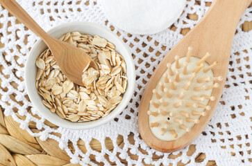 Rolled oats in a small white bowl and wooden hairbrush. Ingredient for preparing homemade face or hair mask. Natural beauty treatment and spa recipe. Top view, copy space.