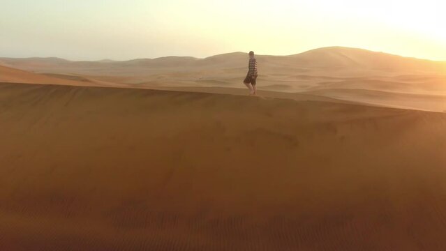 Drone, desert and man walking on dune landscape, sunshine and nature for adventure in summer. Sunset, horizon and sand with explorer, walk and calm in dust, wind or sun for outdoor freedom on travel