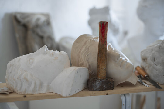 Shot of handcrafted marble busts of greek people and hammer in art studio.