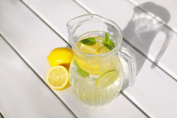 Jug of water with lemons and mint on white wooden table, above view