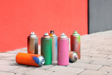 Cans of different spray paints on pavement near wall
