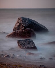 Long exposure vertical shot of waves hitting the rocks located on the shore of a beach