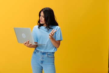 Woman freelancer with a laptop in her hands in a blue t-shirt and jeans on a yellow background smile signs gestures symbols, copy space, free background