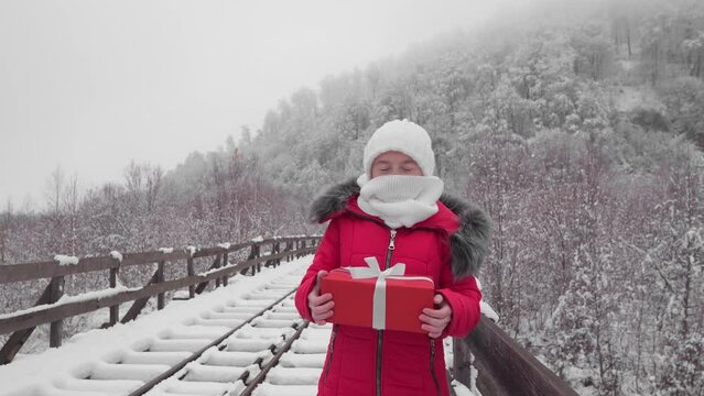 Woman with gift red box on snow. Girl in winter New Year's holidays in December. People outdoors in cold winter. Christmas shopping and a walk through the winter snowy forest in a red cloak.