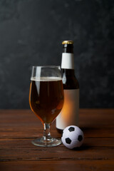 Two glasses with beer, bottles, snacks and soccer ball on wooden table.