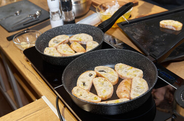 Two frying pans with toasted bread slices on the stove