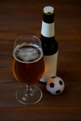 Two glasses with beer, bottles, snacks and soccer ball on wooden table.