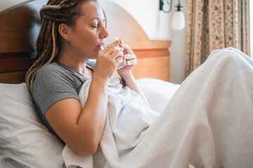 Woman sits in bed and drinks water.