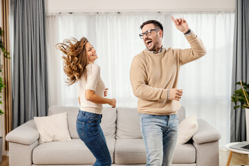 A playful couple is dancing in a living room in their new apartment.