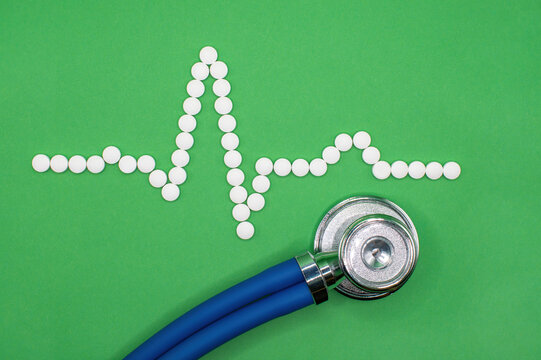 ECG wave form made of medical pills against a green background. A stethoscope sits below the heart trace measuring the Sinus rhythm. Clinical editorial image. EKG Cardiac trace and a healthy heart