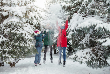 Three happy teen girls are having fun and throws first snow on background of forest. Children play outdoors in snow