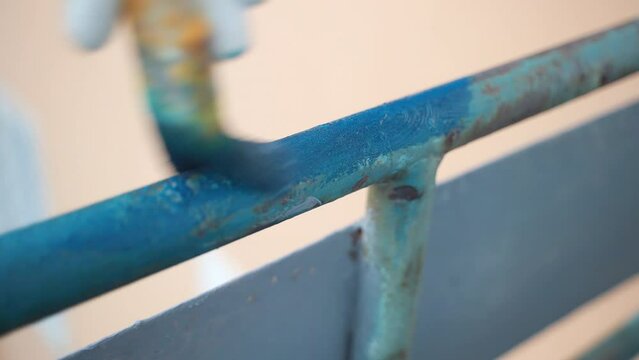 Man painting iron balcony railing with bright blue colour, person covering metal surface after rust and corrosion removal. Process of iron construction restoration and refreshing, painting of old