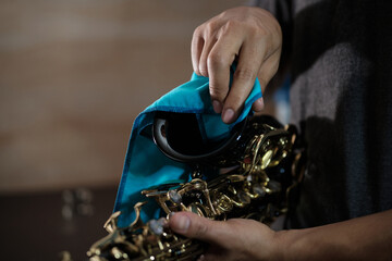 hands of a man wiping the bell of a black saxophone with a cloth