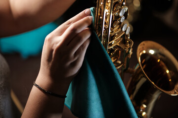 woman's hands cleaning a tenor saxophone with a cloth - obrazy, fototapety, plakaty