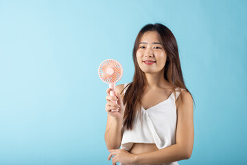 Asian beauty young woman holding pink portable electric mini fan near her face studio shot isolated on blue background, Female hand hold small plastic fan handheld she enjoying cool wind blowing