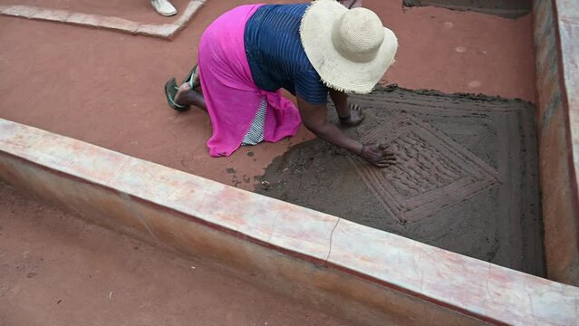 African woman creates a cow dung pattern on the front porch of her home.  An age-old folk art activity
