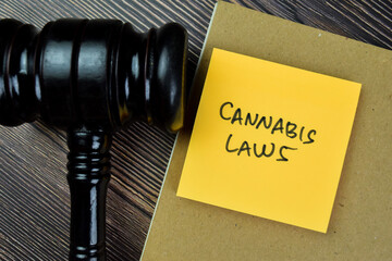 Concept of Cannabis Laws write on sticky notes with gavel isolated on Wooden Table.