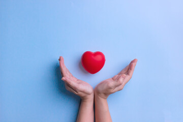 Woman's hand are holding red heart shape to protect and care. Heart world day and Valentine's day concept.