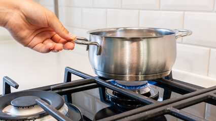Female hand holding saucepan standing on the gas burner of the stove.