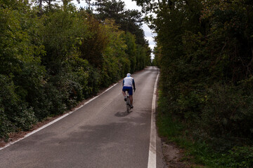 Back view of strong male cyclist riding bike at the paved road