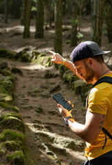 Persona masculina blanca con barba y gorra perdido mirando móvil con mapa o gps buscando el camino.