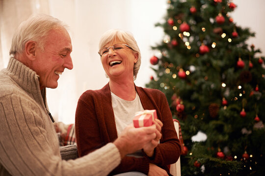 Happy, Love And Old Couple With A Gift For Christmas In Celebration Of A Spiritual Celebration At Home. Smile, Surprise And Senior Woman Enjoys Giving Fancy Presents To An Excited Elderly Partner