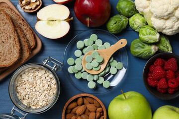 Bowl with pills and foodstuff on blue wooden table, flat lay. Prebiotic supplements