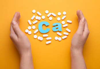 Woman with pills and calcium symbol made of light blue letters on orange background, top view
