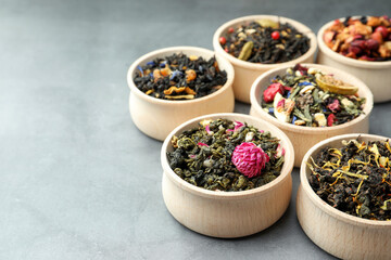 Different kinds of dry herbal tea in wooden bowls on light grey table. Space for text