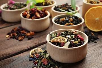 Different kinds of dry herbal tea in bowls on wooden table