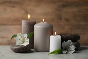 Beautiful composition with burning candles, spa stones and flowers on light grey table