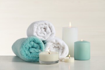Beautiful spa composition with burning candles and rolled towels on white table