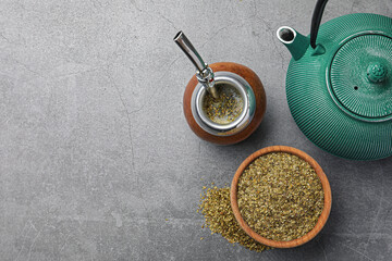 Calabash with bombilla, teapot and bowl of mate tea leaves on grey table, flat lay. Space for text