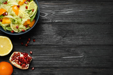 Delicious salad with Chinese cabbage, lemon, persimmon and pomegranate seeds on black wooden table, flat lay. Space for text