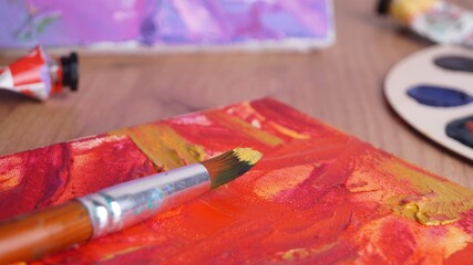 Naklejka na ściany i meble Artist's canvas with mixed paints and brush on wooden table, closeup