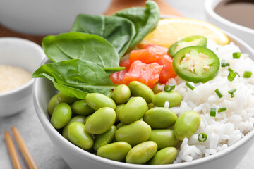 Poke bowl with salmon, edamame beans and rice on light grey table, closeup