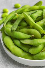 Plate with green edamame beans in pods on light grey table, closeup