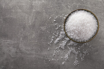 Bowl of natural sea salt on grey table, top view. Space for text