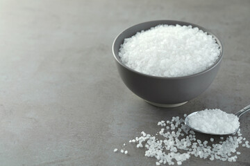 Bowl and spoon with natural sea salt on grey table, space for text