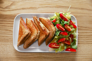 Plate of delicious toasts and salad on wooden table, top view
