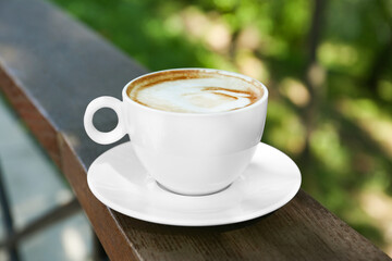 Cup of aromatic coffee on wooden railing outdoors