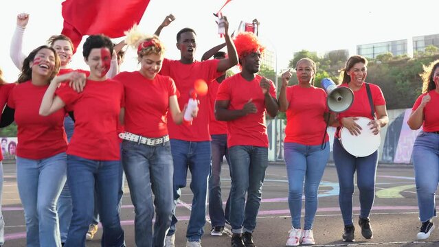 Multiethnic friends football supporter fans watching soccer match at stadium - People with red t-shirts having excited fun on sport world championship event
