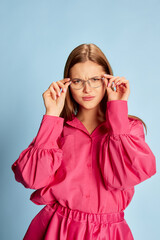 Portrait of young beautiful girl in stylish pink dress posing isolated over blue background. Serious business woman